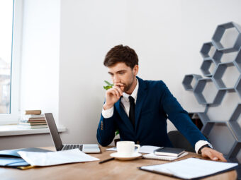 Young successful businessman sitting at workplace, office background.